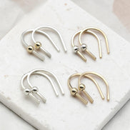 Four minimalist U-shaped hoop earrings with small metallic ball accents, shown in silver and gold finishes arranged on a white marble slab.