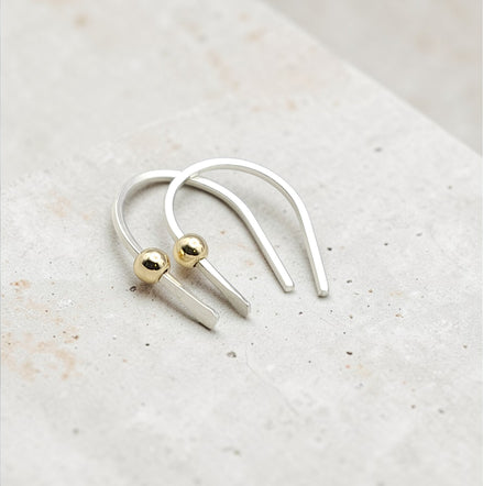 Silver and gold earrings on a light stone surface