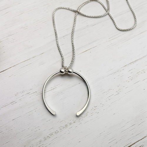 Silver necklace with a unique pendant on a white wooden surface