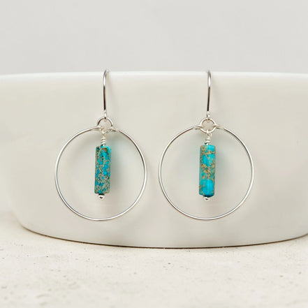 Turquoise bead earrings on silver hooks displayed on a white ceramic dish.