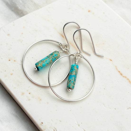 Silver hoop earrings with turquoise beads on a marble surface