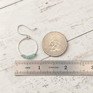 Silver hoop earring with beads next to a coin and ruler on a wooden surface