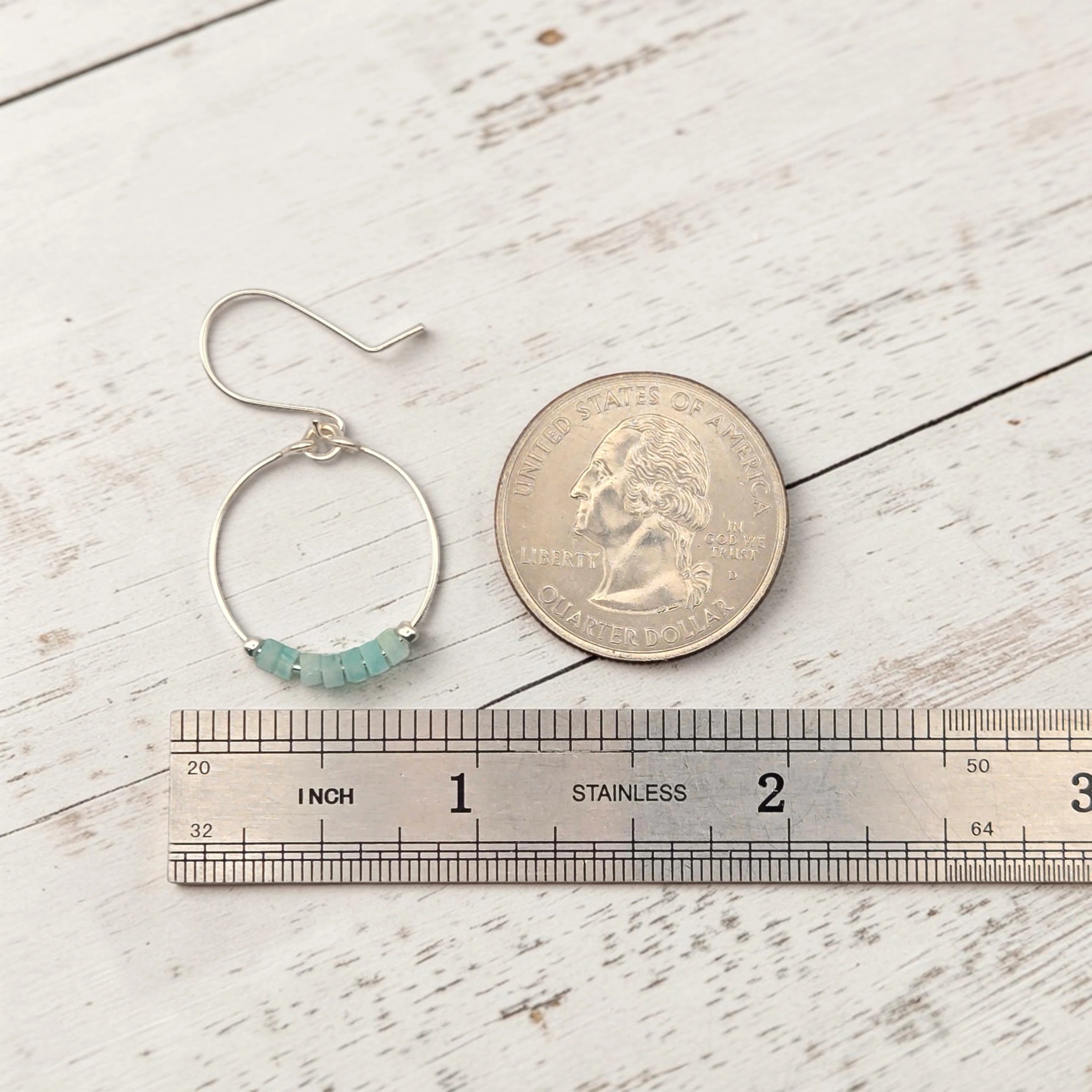 Silver hoop earring with beads next to a coin and ruler on a wooden surface