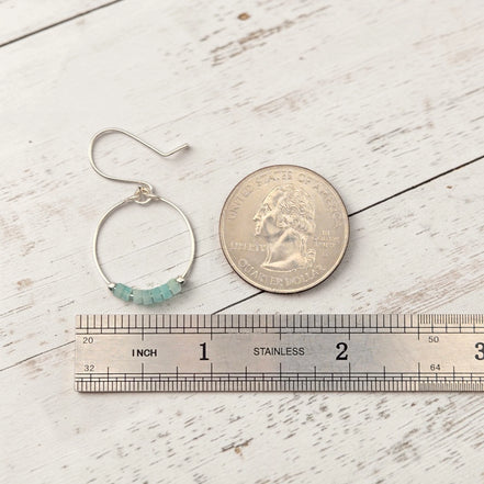 Silver hoop earring with beads next to a coin and ruler on a wooden surface