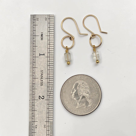 Gold earrings with beads next to a ruler and quarter for scale on a white background