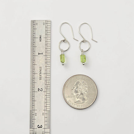 Silver earrings with green beads next to a ruler and quarter for scale on a white background