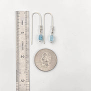 Pair of silver earrings with blue beads next to a ruler and quarter for scale on a white background