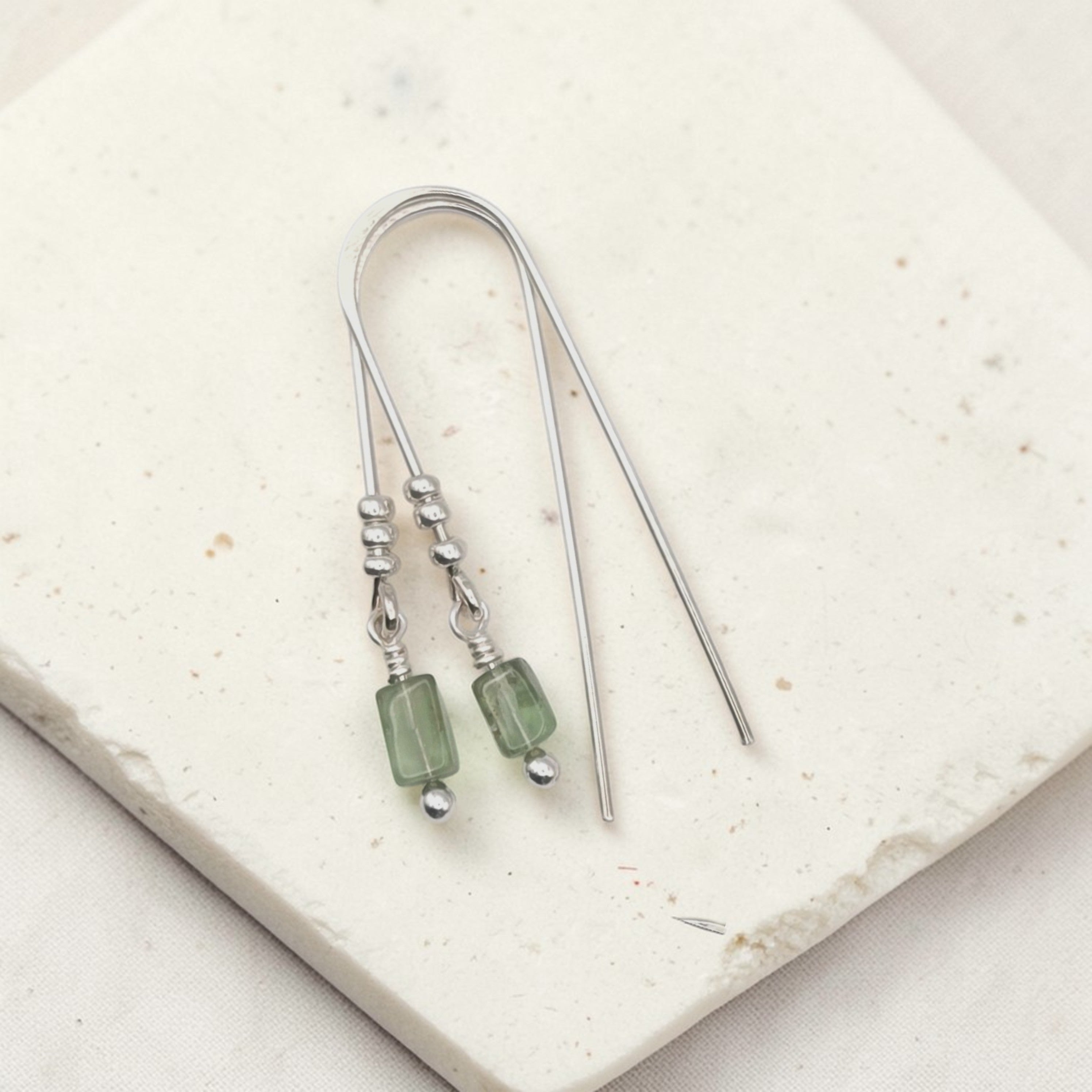 Silver earrings with green beads on a light stone surface