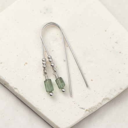 Silver earrings with green beads on a light stone surface