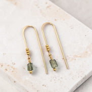 Gold earrings with green beads on a marble surface