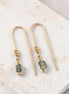 Gold earrings with green beads on a marble surface