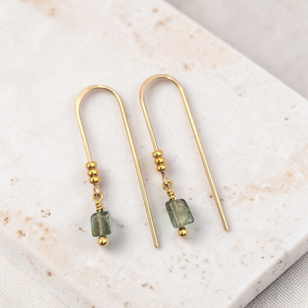Gold earrings with green beads on a marble surface