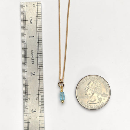 Gold necklace with a blue pendant next to a ruler and a coin for scale on a white background