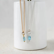 Two necklaces with blue beads hanging from a white vase on a light gray background