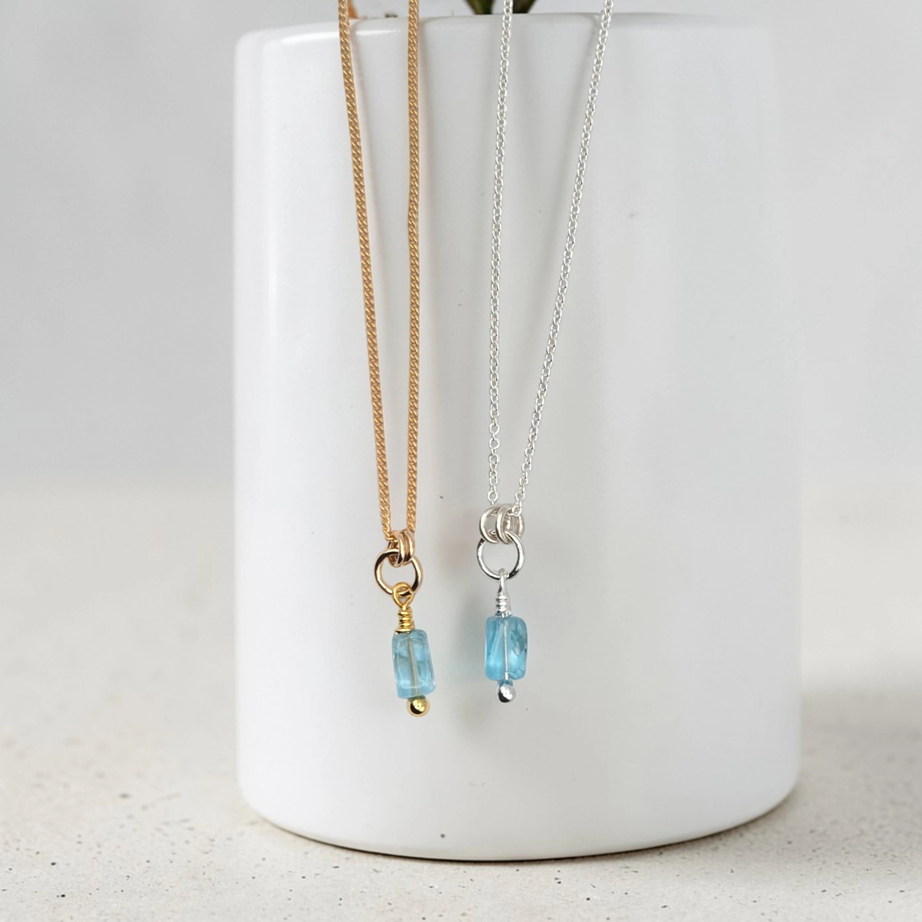 Two necklaces with blue beads hanging from a white vase on a light gray background