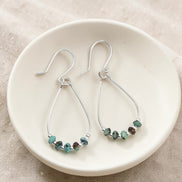 Teardrop-shaped earrings with turquoise beaded details on a white dish.