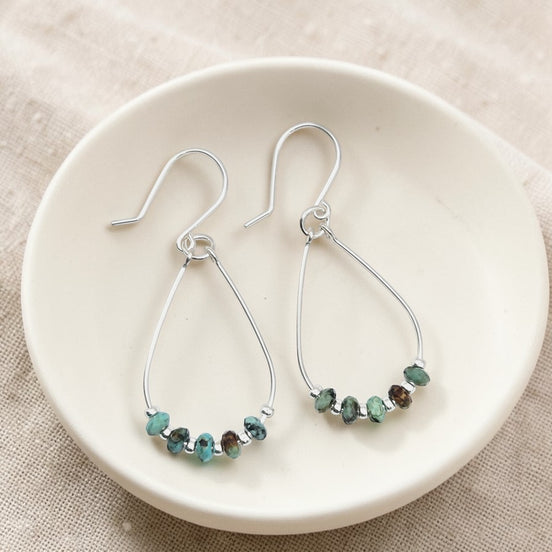 Teardrop-shaped earrings with turquoise beaded details on a white dish.