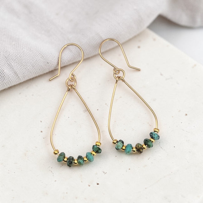 Gold earrings with turquoise beads on a light surface