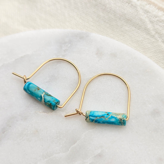 Gold hoop earrings with turquoise beads on a white marble surface