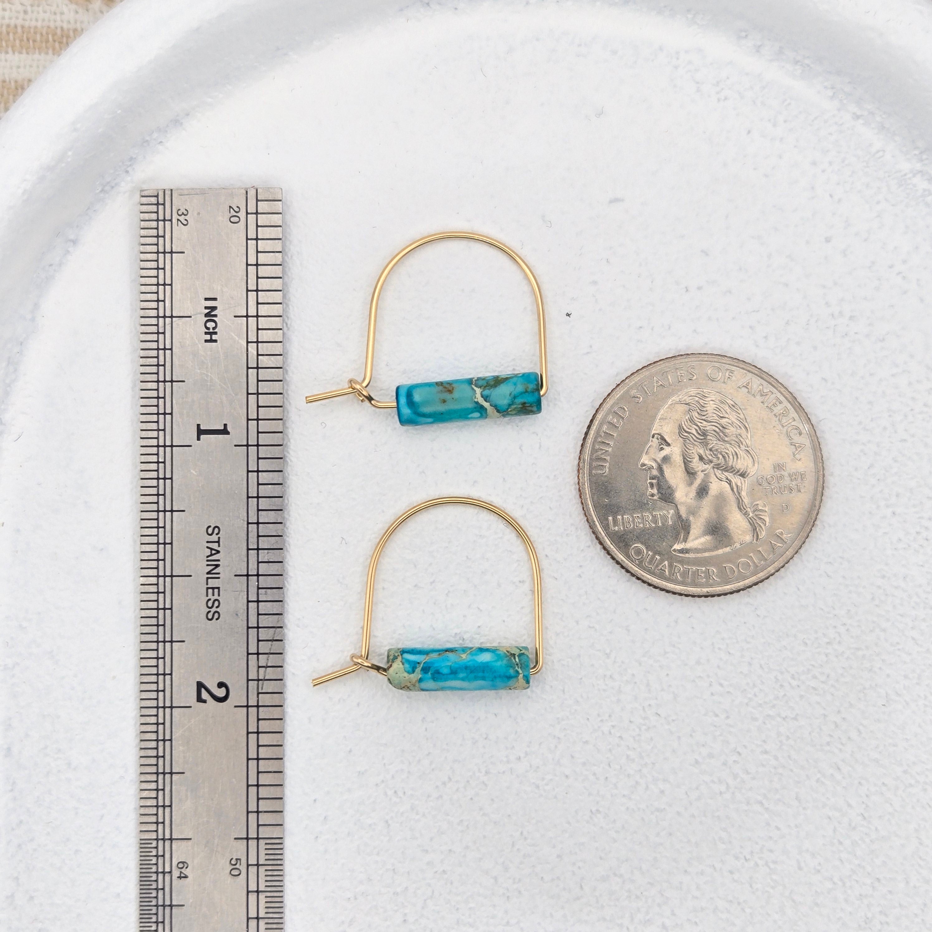 Pair of turquoise bar earrings on a white surface with a quarter and ruler for scale.