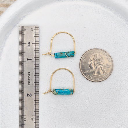 Pair of turquoise bar earrings on a white surface with a quarter and ruler for scale.