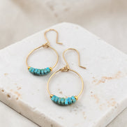 Gold hoop earrings with turquoise beads on a marble surface