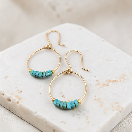 Gold hoop earrings with turquoise beads on a marble surface
