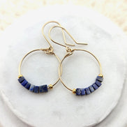 Gold hoop earrings with lapis lazuli beads on a white marble surface