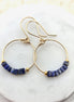 Gold hoop earrings with lapis lazuli beads on a white marble surface
