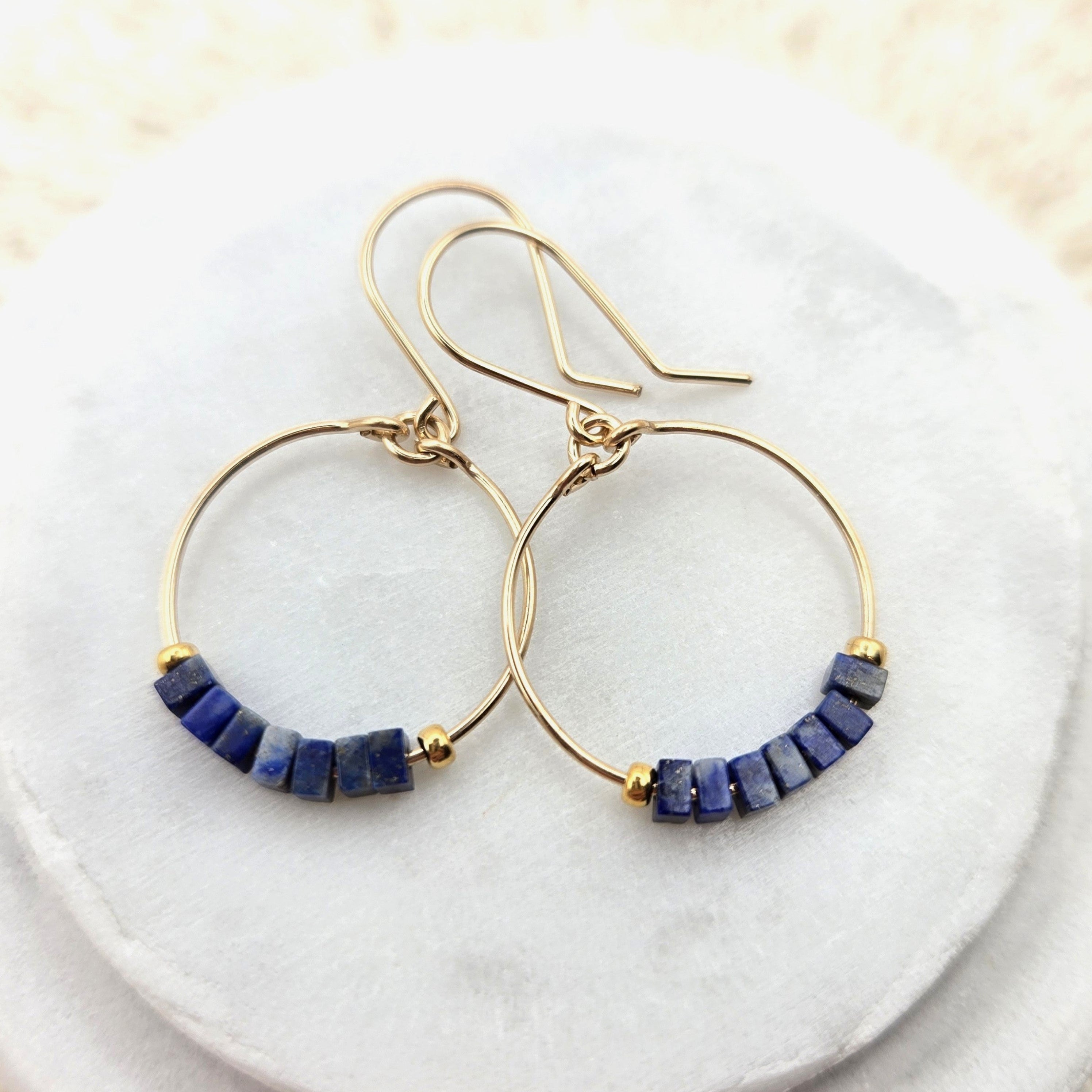 Gold hoop earrings with lapis lazuli beads on a white marble surface