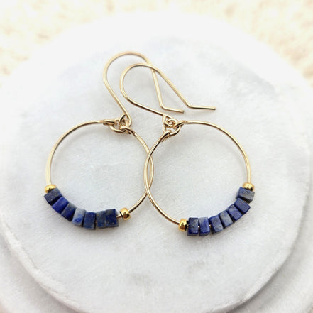 Gold hoop earrings with lapis lazuli beads on a white marble surface