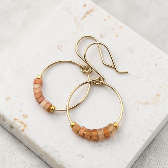 Gold hoop earrings with lrange aventurine beaded accents on a marble surface