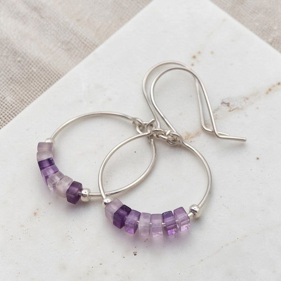 Silver hoop earrings with amethyst purple beads on a marble surface