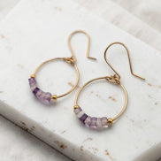 Gold hoop earrings with purple beads on a marble surface