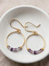 Gold hoop earrings with purple beads on a white dish.