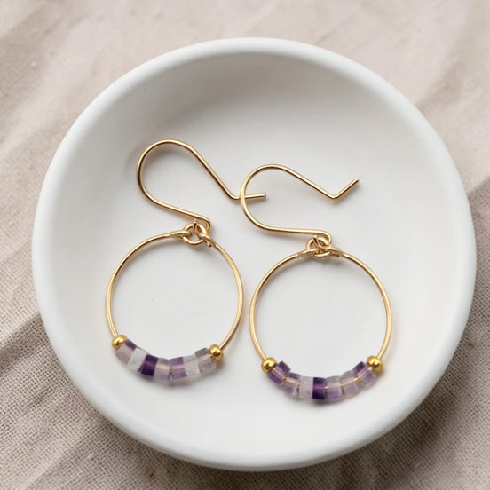 Gold hoop earrings with purple beads on a white dish.