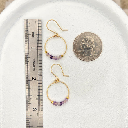 Amethyst hoop earrings on a white surface with a coin and ruler for scale.