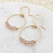 Gold hoop earrings with pink gemstones on a white surface