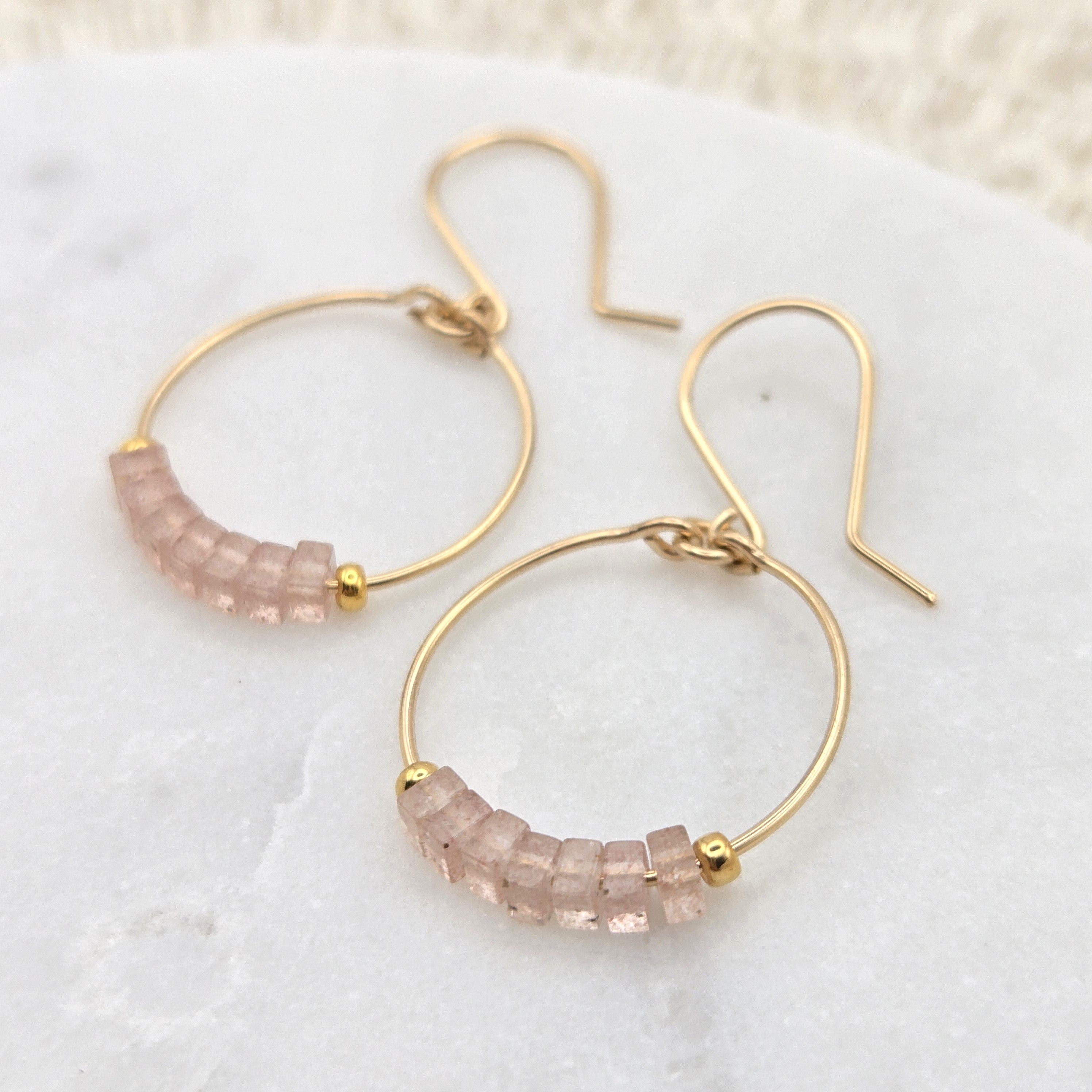 Gold hoop earrings with pink gemstones on a white surface