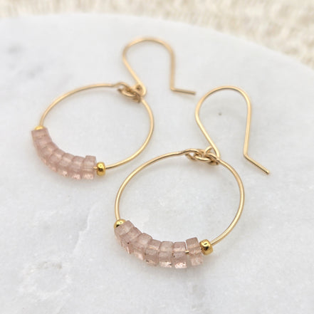 Gold hoop earrings with pink gemstones on a white surface