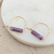 Gold hoop earrings with amethyst beads on a white plate.