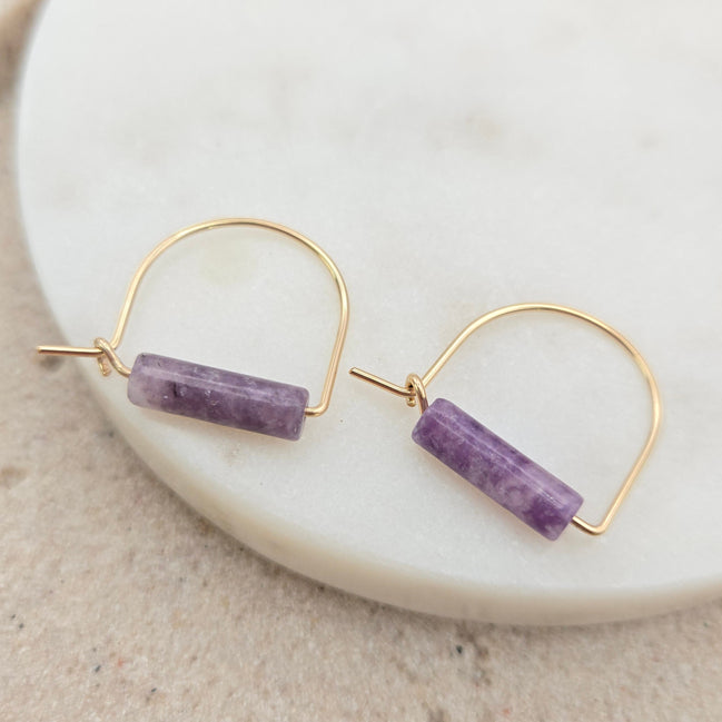 Gold hoop earrings with amethyst beads on a white plate.