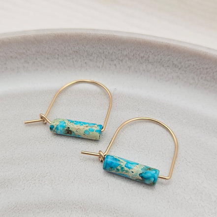 Gold hoop earrings with turquoise cylindrical beads on a light gray background