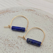 Gold hoop earrings withlapis lazuli beads on a light gray background