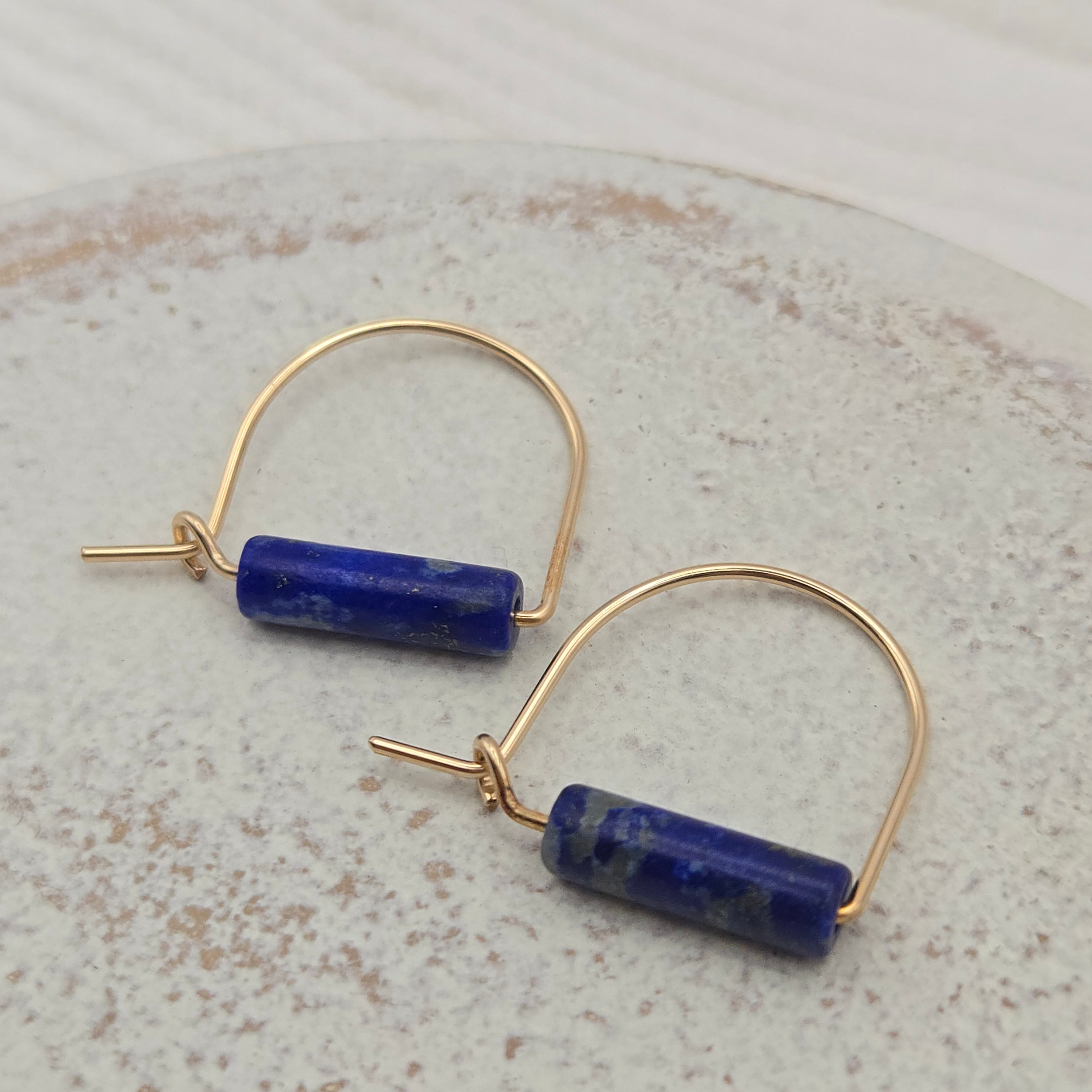 Gold hoop earrings withlapis lazuli beads on a light gray background