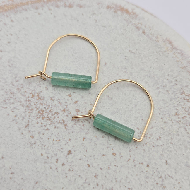 Gold hoop earrings with green cylindrical beads on a textured surface