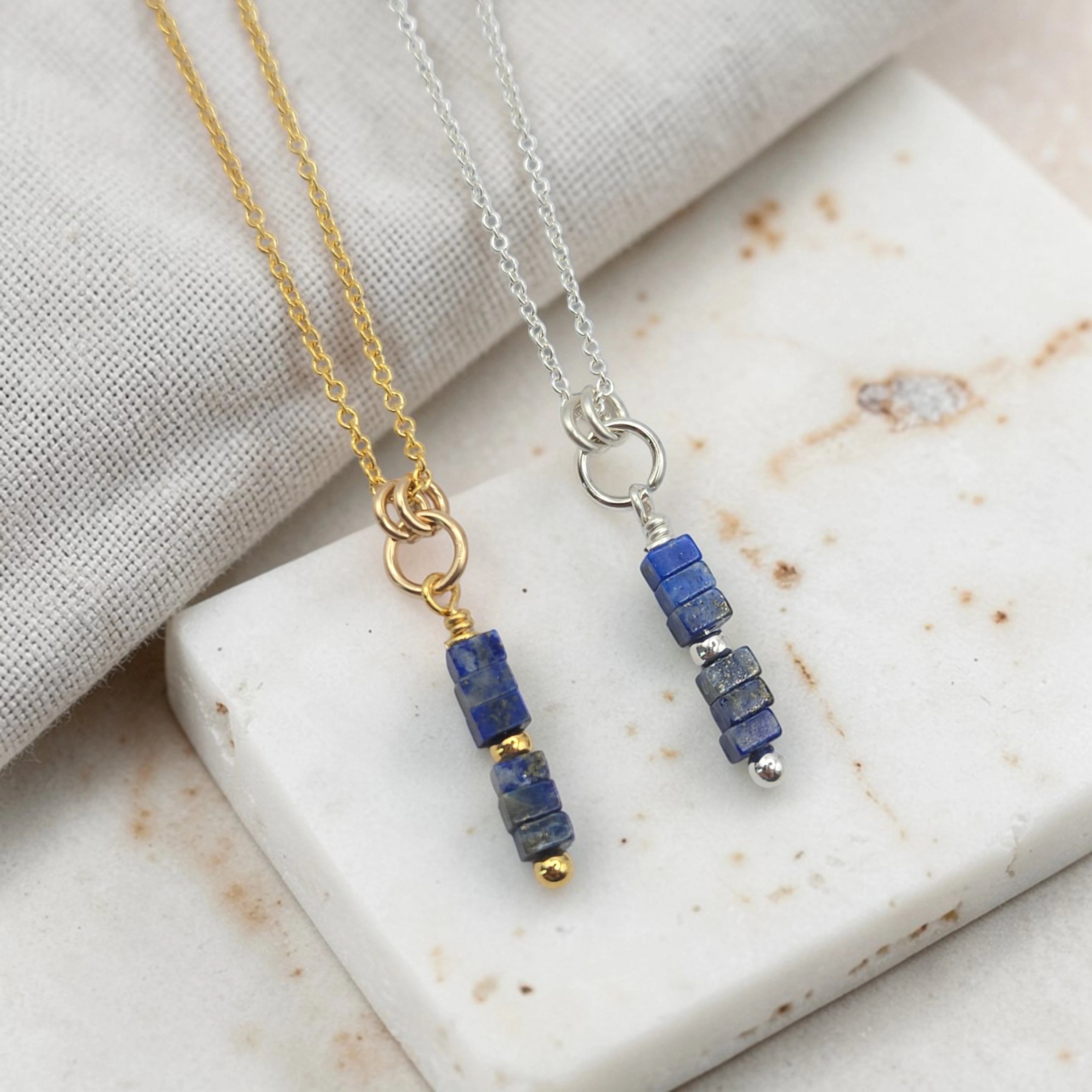 Two necklaces with blue bead pendants on a marble surface.