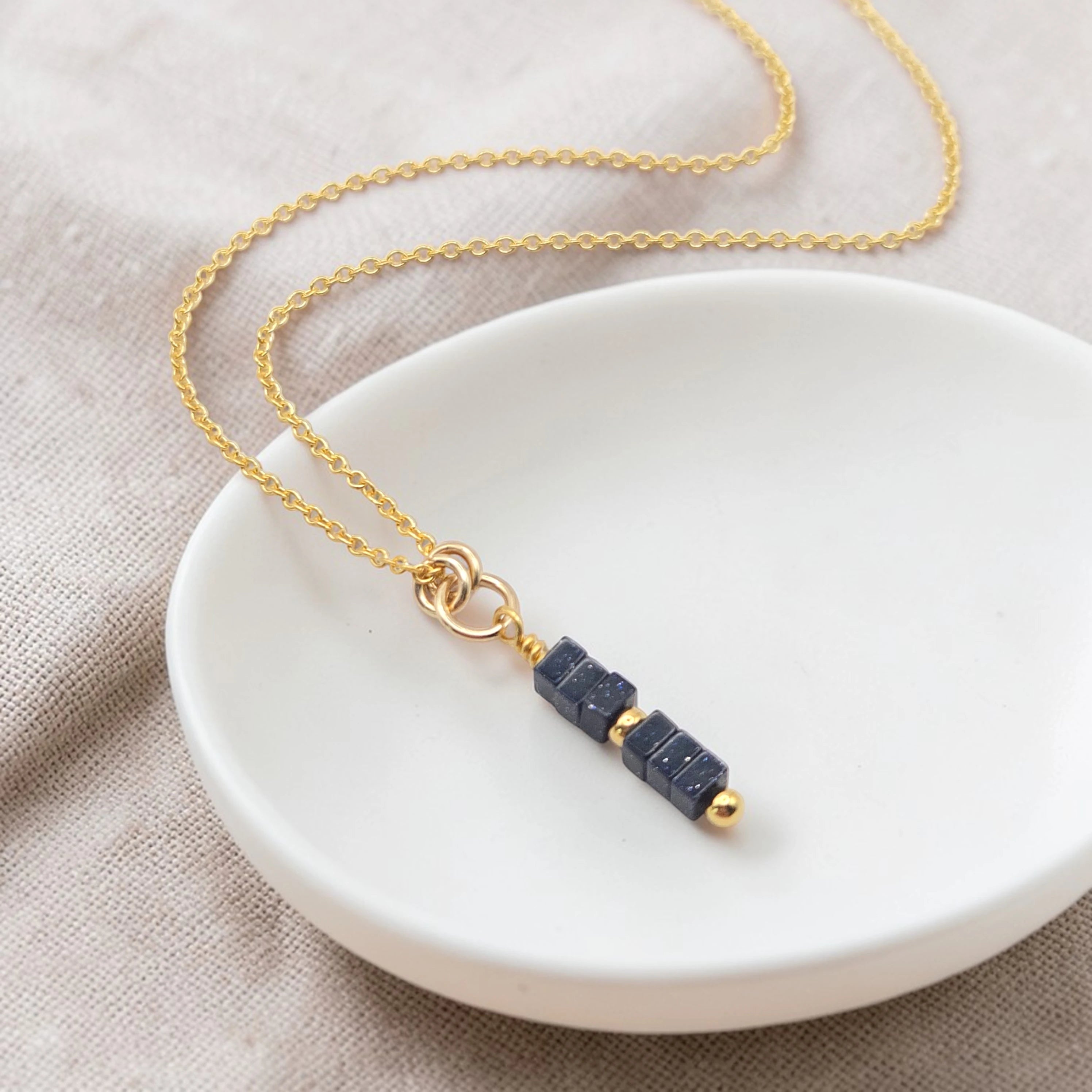 Necklace with blue beads and gold chain on a white dish