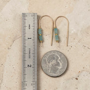 Gold earrings with blue beads next to a ruler and quarter for scale on a beige surface