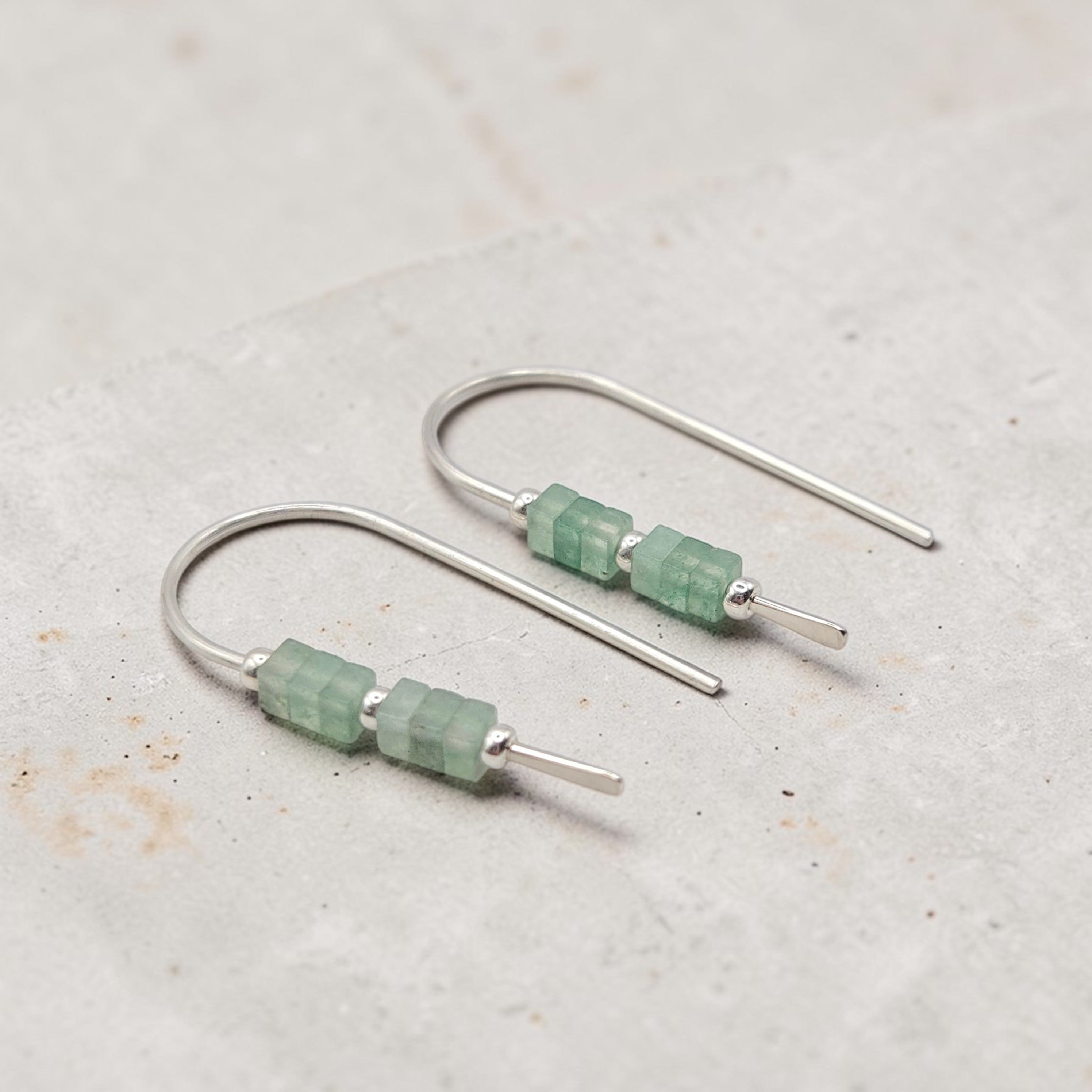 Silver earrings with green beads on a light gray background